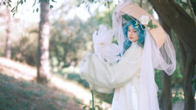 Cosplayer in elaborate costume with blue hair and floral accents set in a serene outdoor environment.