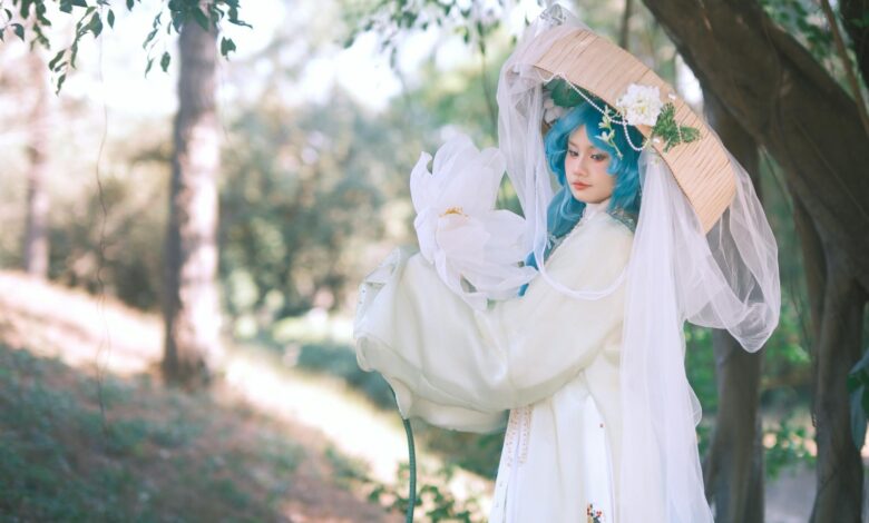 Cosplayer in elaborate costume with blue hair and floral accents set in a serene outdoor environment.