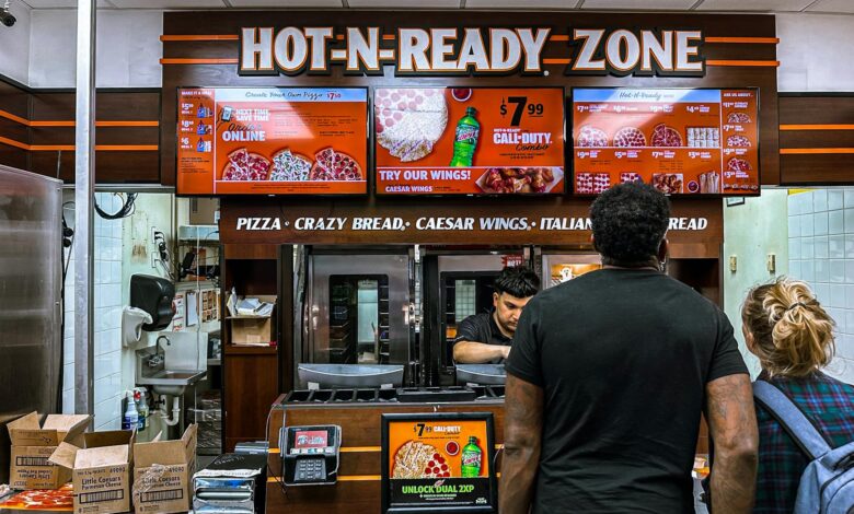 Busy fast food restaurant with customers ordering pizza at the counter under bright digital menu signage.