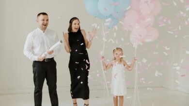 A family celebrates a gender reveal with balloons and confetti indoors.