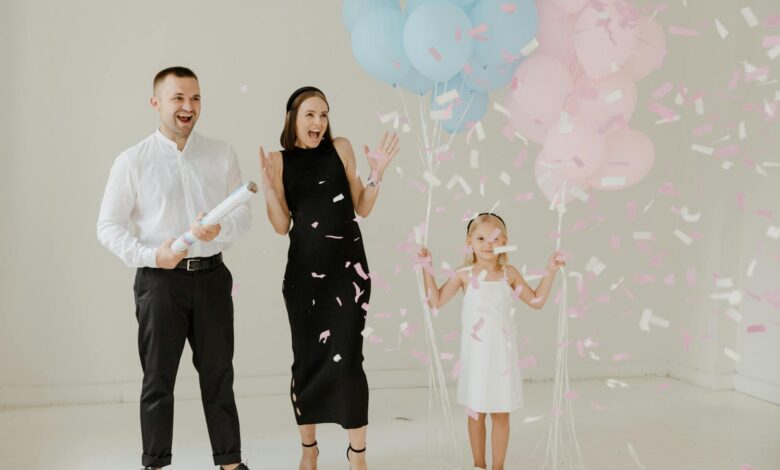 A family celebrates a gender reveal with balloons and confetti indoors.