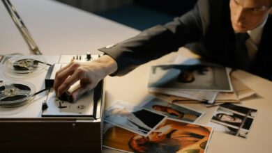 A detective adjusting a tape recorder during an investigation with photos spread on a table.