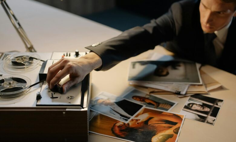 A detective adjusting a tape recorder during an investigation with photos spread on a table.