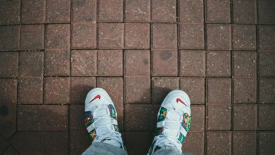 Top-down view of trendy white sneakers with colorful design on a red brick walkway.
