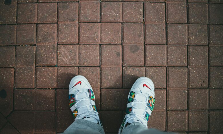 Top-down view of trendy white sneakers with colorful design on a red brick walkway.