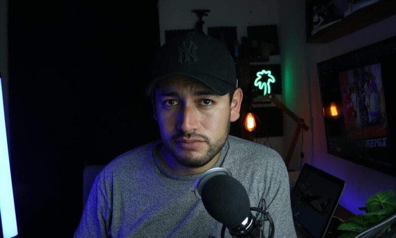 Male content creator in a home studio setup with microphone and soft lighting.