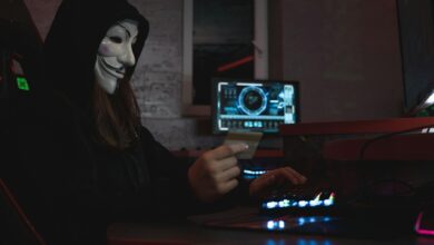 Masked hacker with credit card at computer, symbolizing cybercrime and anonymity.