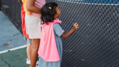 Kids wearing colorful capes watch eagerly through a fence, capturing the joy of outdoor play.