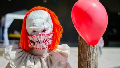 A person in a scary clown costume with a red balloon outdoors, perfect for Halloween themes.