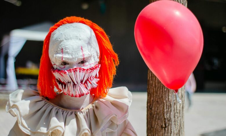 A person in a scary clown costume with a red balloon outdoors, perfect for Halloween themes.