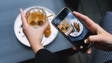 Hands taking a photo of iced coffee and croissant with a smartphone, perfect for food bloggers.