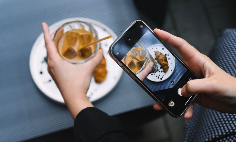 Hands taking a photo of iced coffee and croissant with a smartphone, perfect for food bloggers.