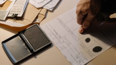 Detailed view of a hand taking fingerprints on a document with ink pad on desk.