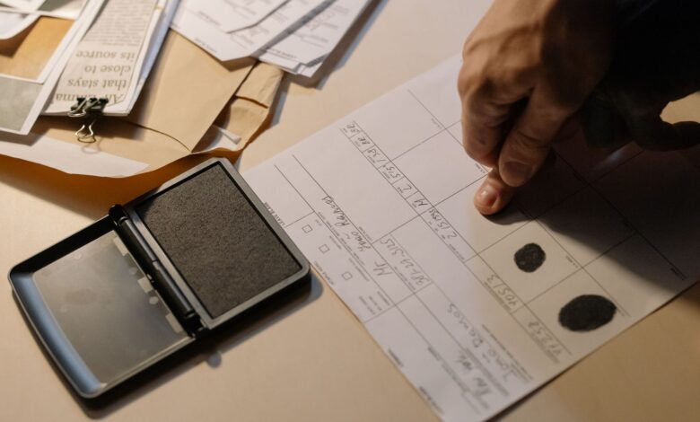 Detailed view of a hand taking fingerprints on a document with ink pad on desk.