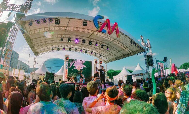 Colorful outdoor music festival with a lively crowd enjoying live performances under a sunny sky.
