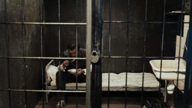 A prisoner sits alone in a dark cell, eating with focus in a moody environment.