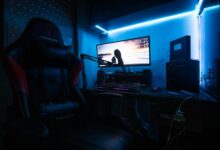 A sleek gaming desk with a monitor, gaming chair, and LED lights creating an immersive environment.