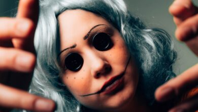 Creepy close-up of a woman in disguise, featuring button eyes and a painted face for a horror effect.