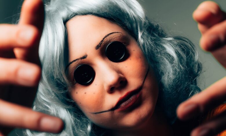 Creepy close-up of a woman in disguise, featuring button eyes and a painted face for a horror effect.