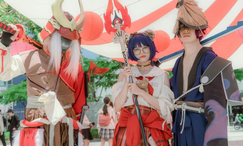Three cosplayers dressed as fantasy characters pose together under vibrant canopy outdoors.