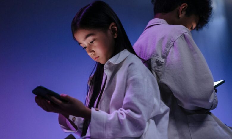 Two children engrossed in using their smartphones in a dimly lit setting.