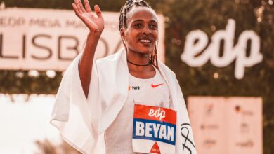 Triumphant female marathon runner celebrates victory wrapped in towel outdoors.