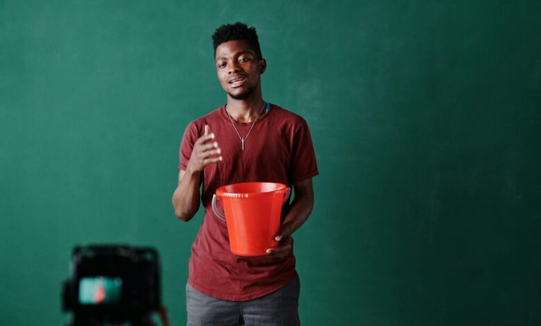 African American man holding a red bucket, presenting in front of a green background.