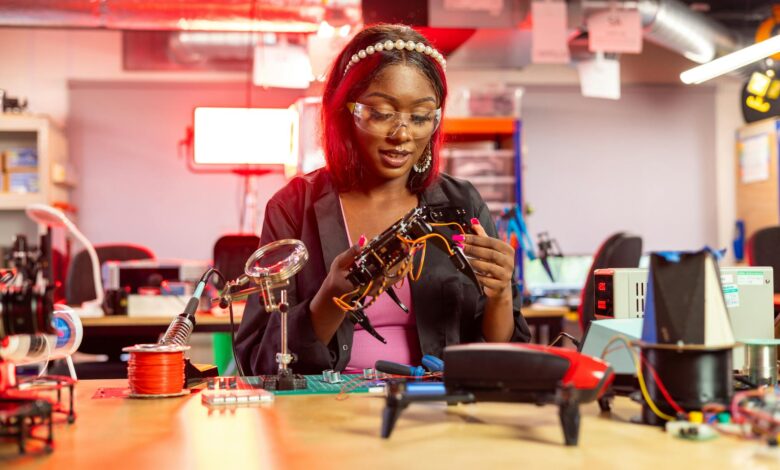 Black female engineer at desk assembling drones, showcasing electronics and technology in a modern lab setting.