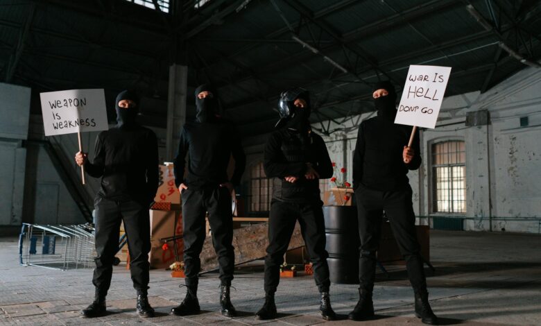 Four masked protesters stand indoors with anti-war signs, advocating peace.