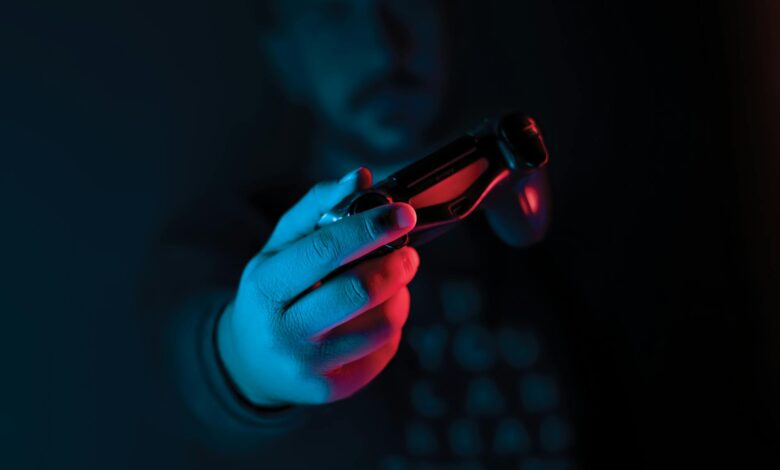 Close-up of a man's hand holding a joystick against a dark background with red and blue lighting.