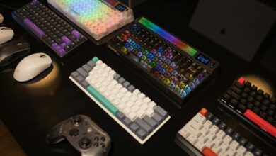 A collection of mechanical keyboards and gaming accessories displayed on a table, illuminated by vibrant RGB lighting.