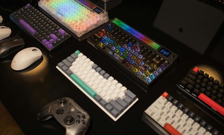 A collection of mechanical keyboards and gaming accessories displayed on a table, illuminated by vibrant RGB lighting.
