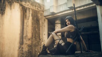 A woman in tactical gear poses in an abandoned urban setting, exuding strength and mystery.