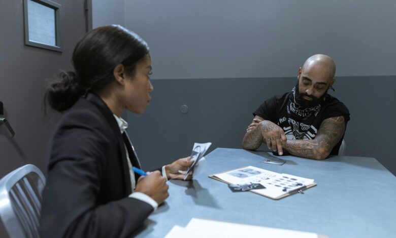 Police officer interrogating a suspect in an investigation room with documents and evidence on the table.
