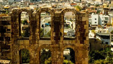 View of ancient stone ruins with a cityscape in the background, showcasing Athens' historic architecture.