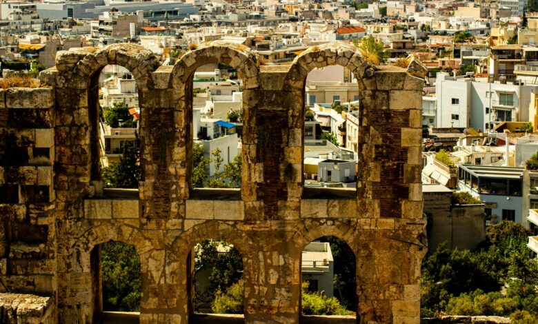 View of ancient stone ruins with a cityscape in the background, showcasing Athens' historic architecture.