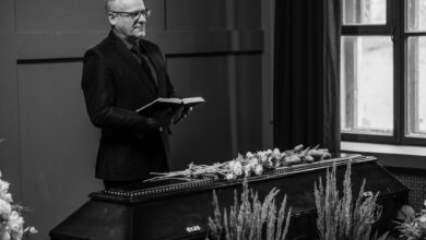 A solemn indoor funeral ceremony with a pastor standing beside a coffin.