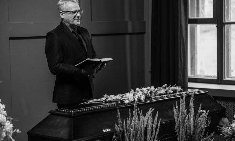 A solemn indoor funeral ceremony with a pastor standing beside a coffin.