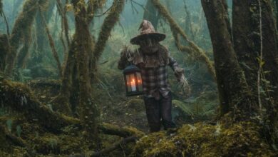 A person in a scarecrow costume holding a lantern among foggy trees in Choachí, Colombia.