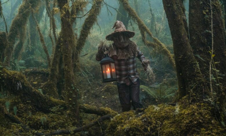 A person in a scarecrow costume holding a lantern among foggy trees in Choachí, Colombia.
