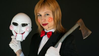 Woman in horror-themed costume holding an axe and mask, suited for Halloween.