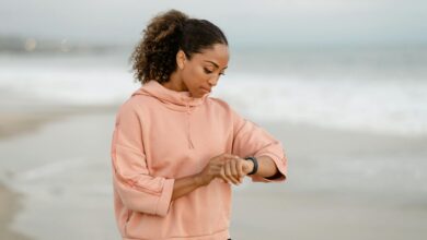 A woman in casual attire checks her smartwatch while standing on a sandy beach.