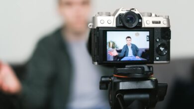 Man recording a vlog indoors using a mirrorless camera on a tripod with selective focus.