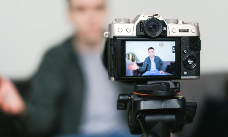 Man recording a vlog indoors using a mirrorless camera on a tripod with selective focus.