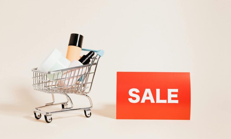 A miniature shopping cart filled with products beside a bright sale sign, ideal for retail and marketing concepts.