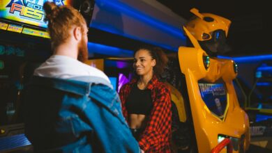 Happy couple holding hands and smiling in a vibrant arcade setting.