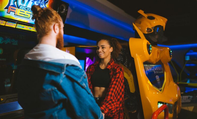 Happy couple holding hands and smiling in a vibrant arcade setting.