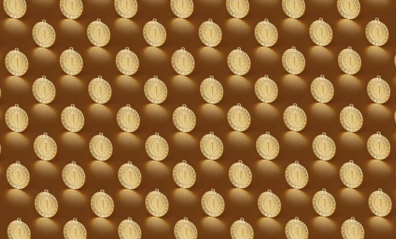 Multiple gold medals arranged in a repeating pattern on a brown backdrop.