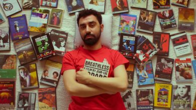 Man in red t-shirt surrounded by various DVD covers laying on a textured wall.