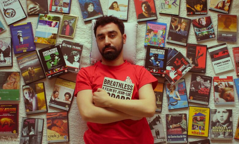 Man in red t-shirt surrounded by various DVD covers laying on a textured wall.